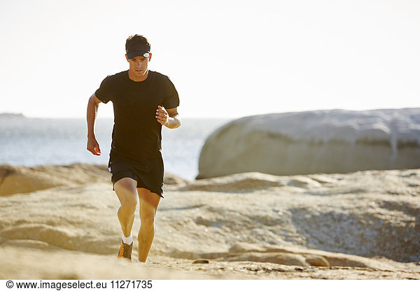 Male triathlete running on sunny rocky trail