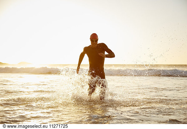 Male triathlete running out of ocean