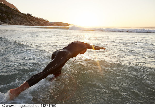 Male triathlete swimmer in wet suit diving into ocean
