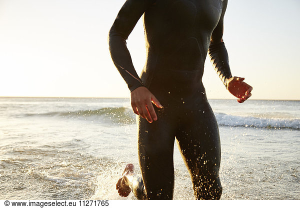 Male triathlete swimmer in wet suit running out of ocean surf