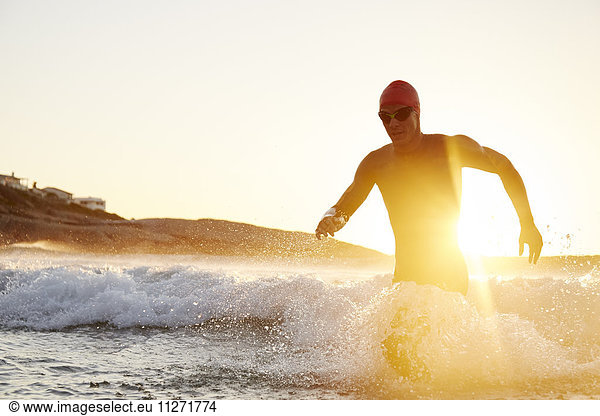 Male triathlete swimmer in wet suit running out of sunny ocean