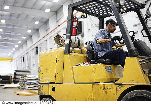 Male worker driving forklift in warehouse