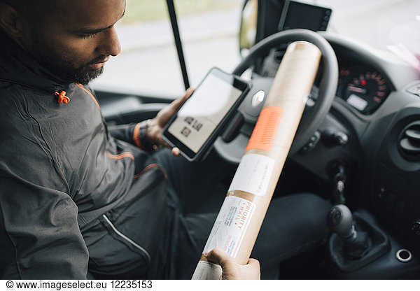 Male worker examining package while using digital tablet in delivery van