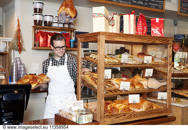 Male worker in bakery  putting fresh goods into display cabinet
