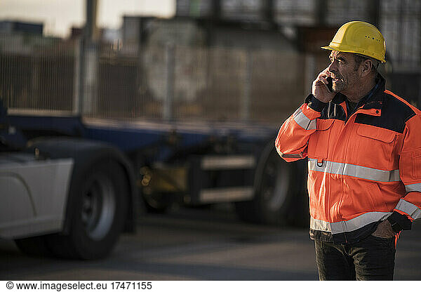 Male worker with hand in pocket talking on smart phone at commercial dock