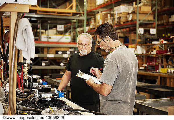 Male workers checking papers while standing by table in warehouse