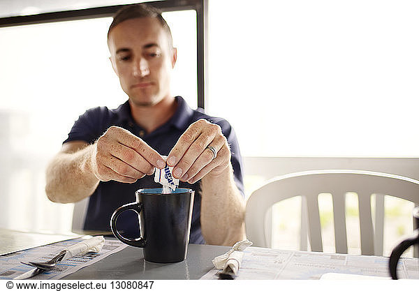 Man adding sugar to coffee mug at restaurant table