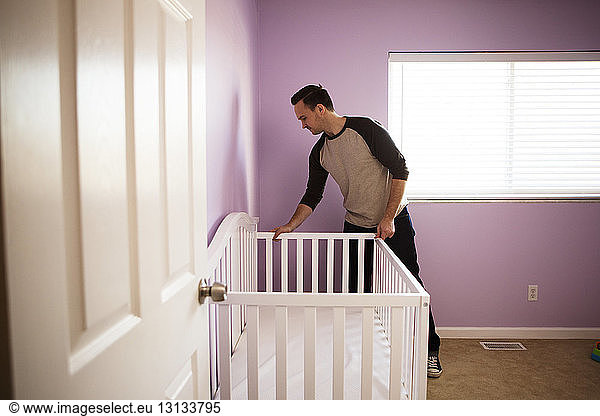 Man adjusting crib at bedroom against wall