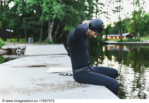 Man adjusting swimming cap sitting by lake