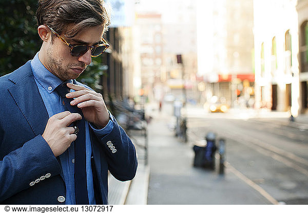 Man adjusting tie while standing at city street