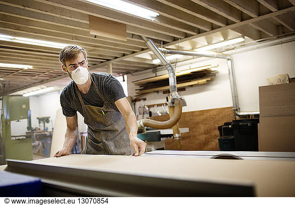 Man adjusting wooden plank on table while working in workshop
