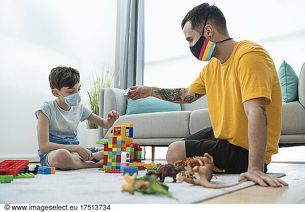 Man and boy wearing masks while playing with toy blocks in living room during Covid-19 curfew