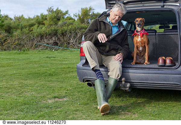 Man and dog sitting in car boot removing wellington boots