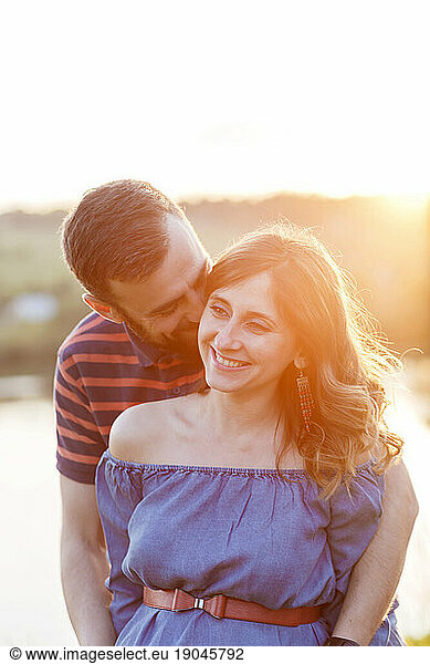 man and pregnant woman in dress are hugging in summer at sunset