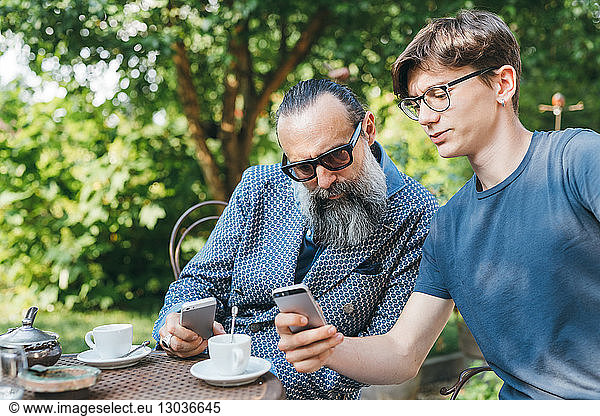 Man and son using cellphone over coffee in garden