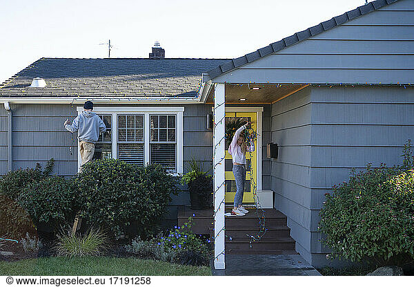 Man and tween girl decorating a residential house with holiday lights