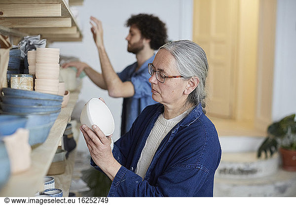 Man and woman arranging earthenware on shelf in art class