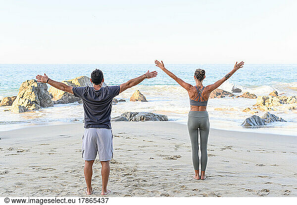 Man and woman doing yoga at sunrise on the beach