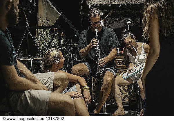 Man and woman playing musical instruments while sitting with friends at resort