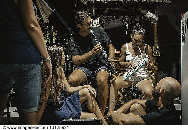 Man and woman playing musical instruments while sitting with friends at tourist resort