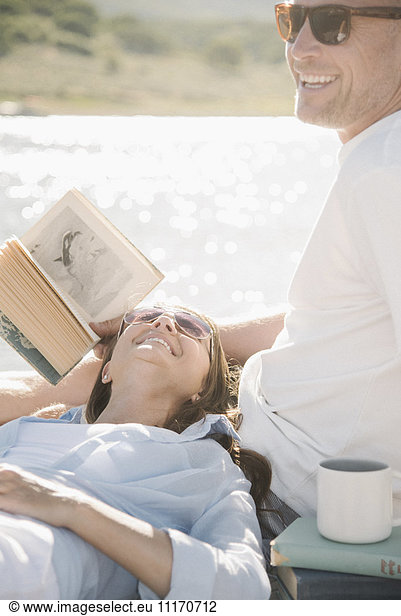 Man and woman reclining on a jetty  reading a book.