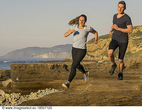 Man and woman running on single trail on coast of Azkorri beach