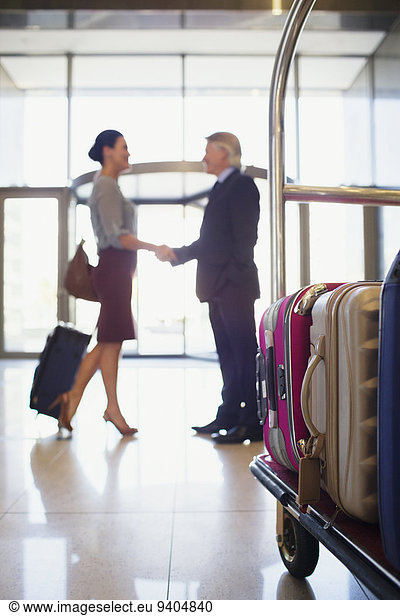 Man and woman shaking hands in hotel lobby  luggage cart in foreground