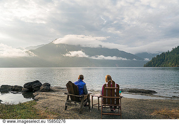 Man and woman sitting at edge of lake during sunset