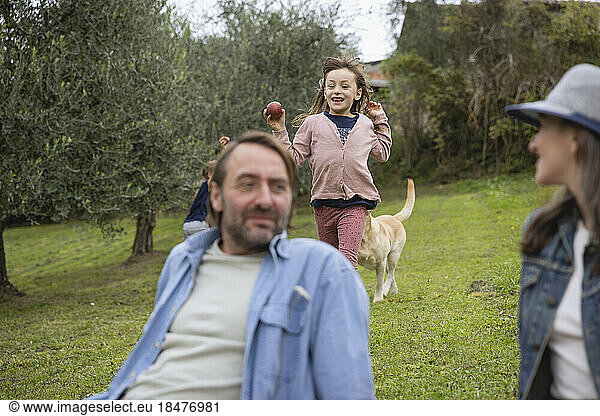 Man and woman sitting on grass with daughter running in background