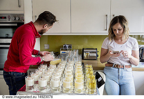 Man and woman standing in a domestic kitchen  making jar candles.