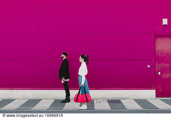 Man and woman standing on a pink wall  looking away