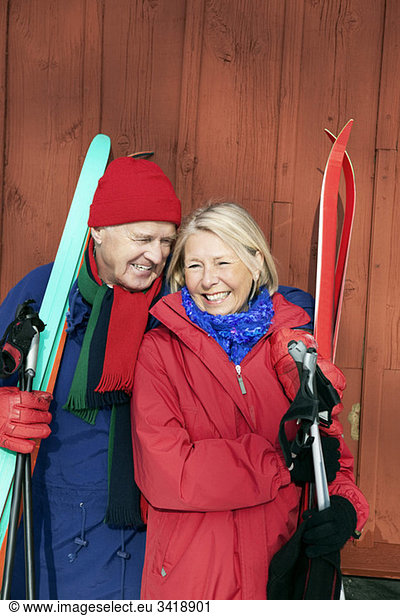 Man and woman standing outdoors holding skis