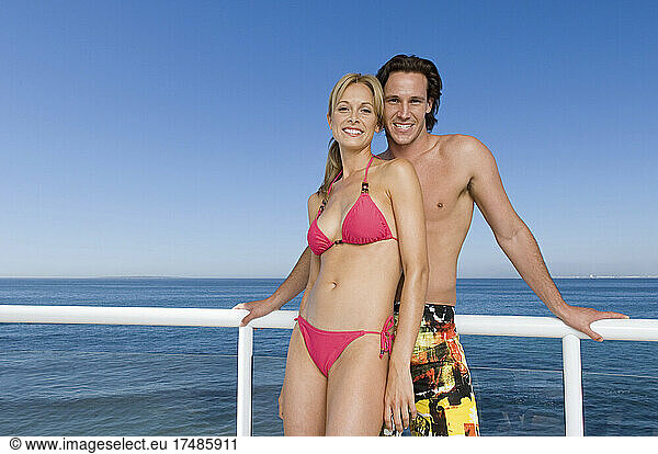 Man and woman standing together at the rail of a cruise ship wearing swimwear.