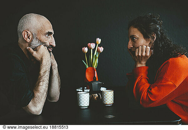 Man and woman staring each other sitting with leaning on elbows at table