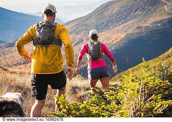 Man and woman trail running with dog in mountains at sunrise