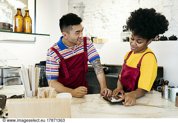Man and woman using tablet PC leaning on checkout counter in cafe