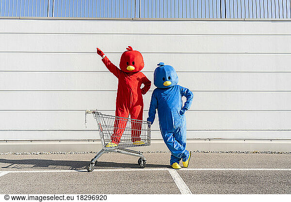 Man and woman wearing duck costumes standing with shopping cart in front of wall