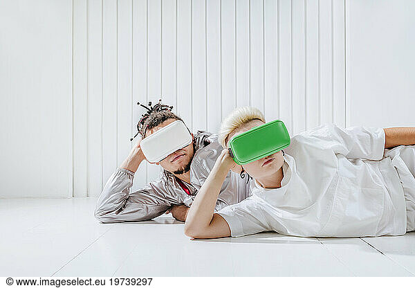 Man and woman wearing virtual reality headset lying on side in front of white wall