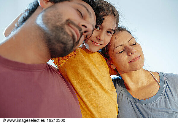 Man and woman with eyes closed embracing daughter at home