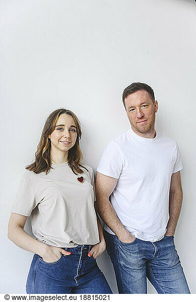 Man and woman with hands in pockets standing against white background