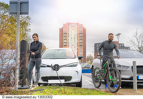 Man and woman with mountain bike at electric car charging point  Manchester  UK