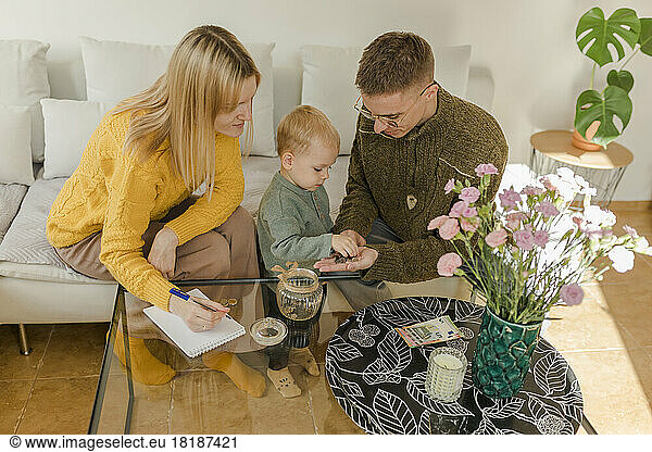 Man and woman with son counting coins in living room at home