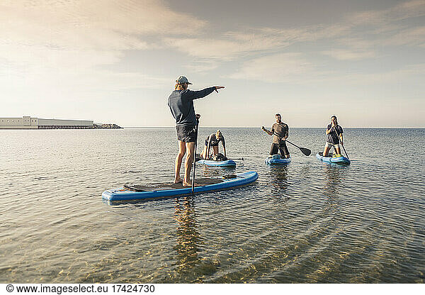 Man and women learning to row paddleboard from male instructor in sea