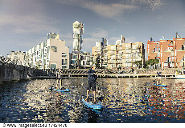 Man and women paddleboarding in sea against buildings