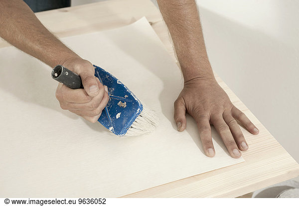 Man applying glue on wallpaper with a brush