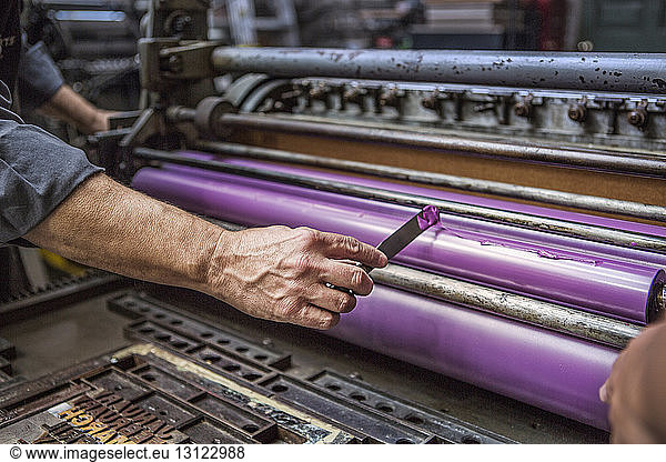 Man applying purple ink on printing roller at workshop