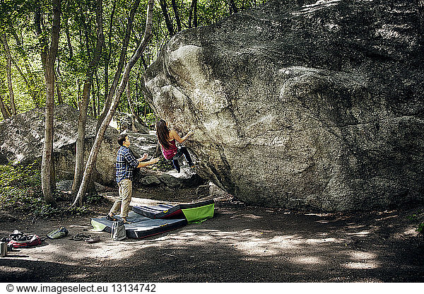 Man assisting woman in climbing rock at forest