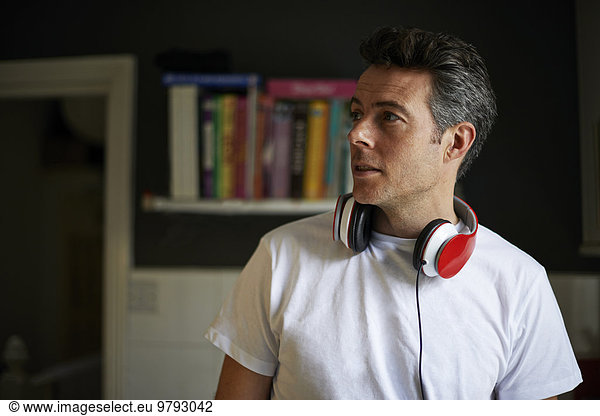 Man at home with red headphones over his neck looking away