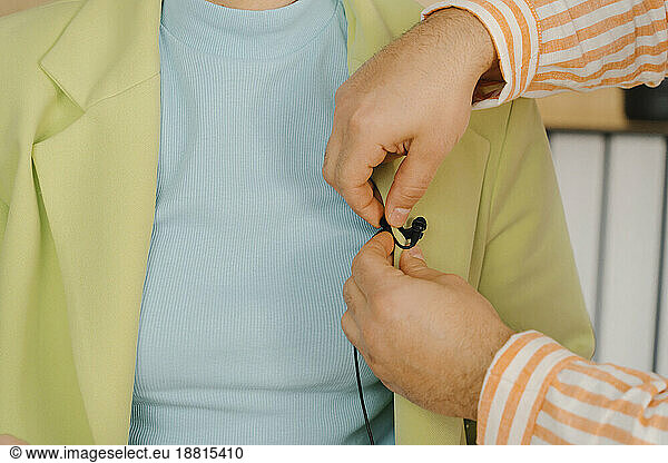 Man attaching a lavalier microphone to a woman's jacket