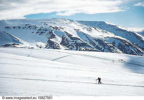Man backcountry skiing on ski tracks with mountain in background